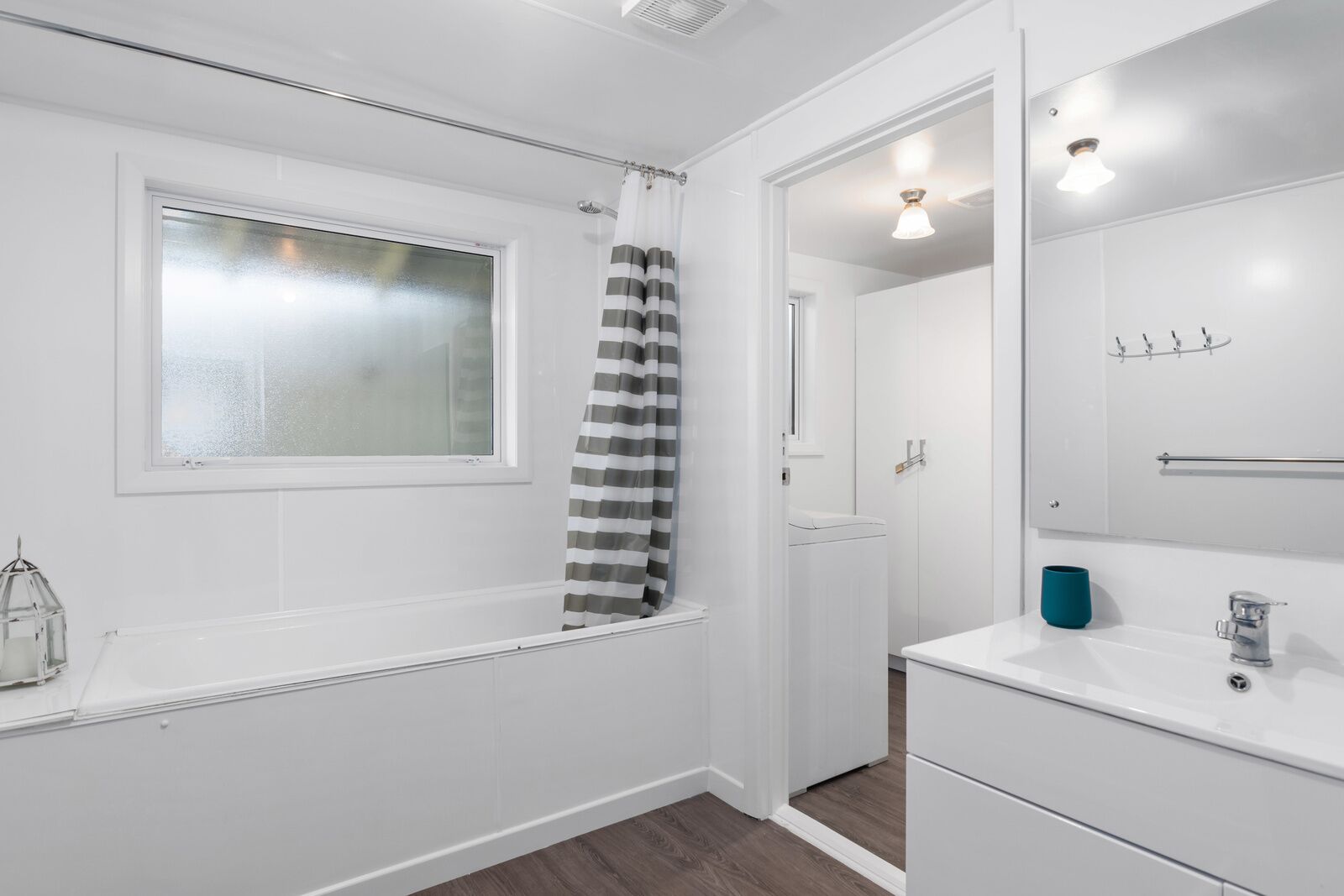 A modern bathroom with a bathtub, a window, a shower curtain, a sink, and a mirror.