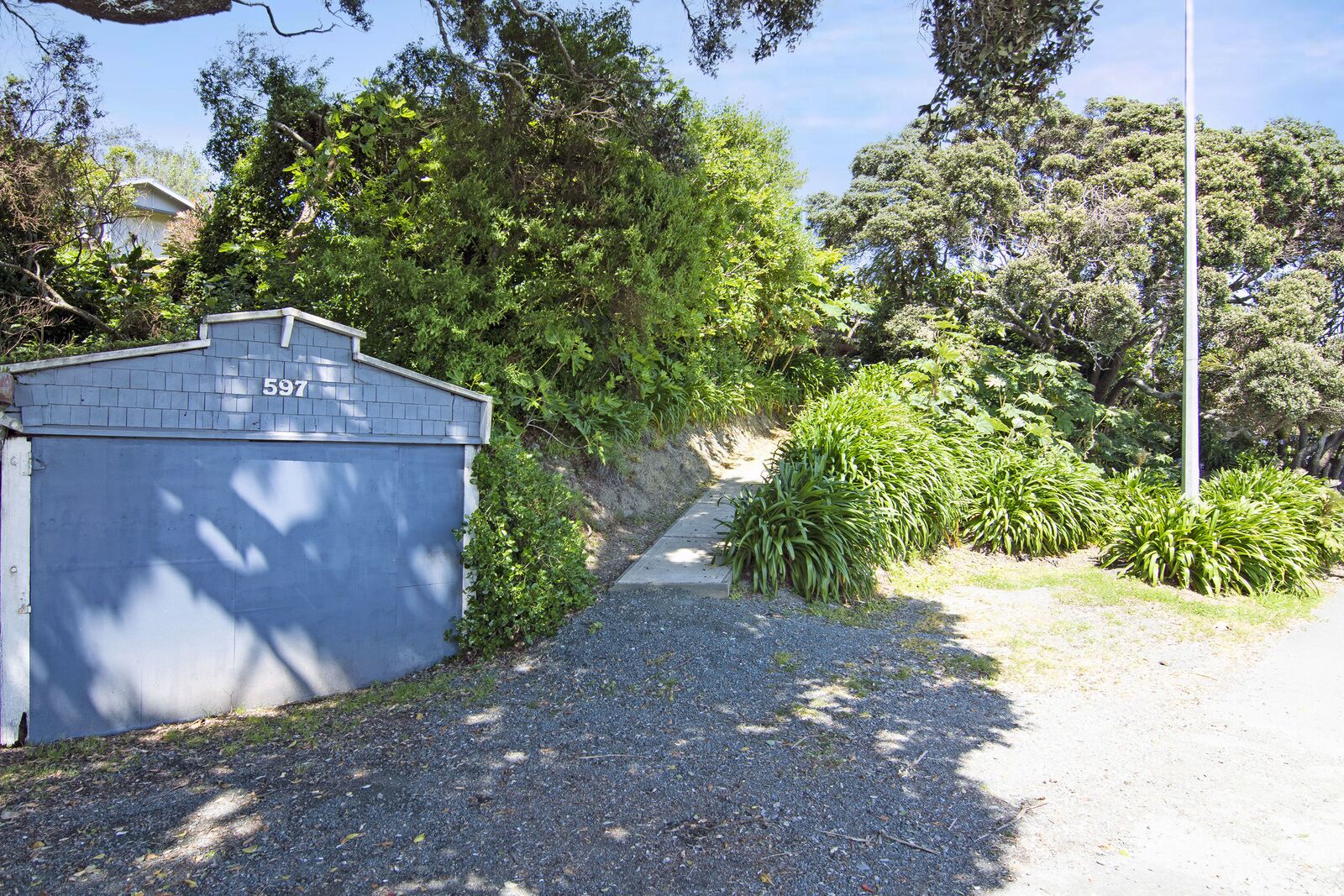 A residential driveway with a blue garage, number 597, surrounded by lush greenery and trees.