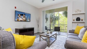 Una sala de estar con un sofá gris, almohadas amarillas, una mesa de centro y un televisor montado en la pared.