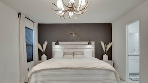 Ein modernes Schlafzimmer mit einem großen Bett, einer dekorativen Deckenleuchte und Blick ins Freie.