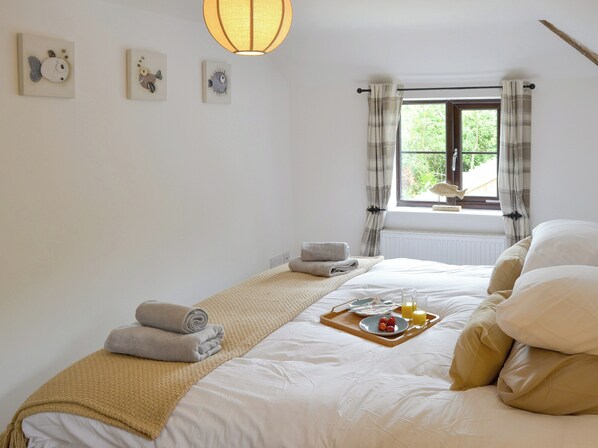 A neatly made bed with a tray of breakfast items, a window with curtains, and wall art.