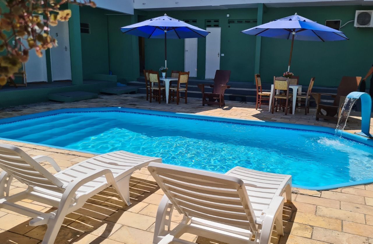 Una piscina con sillas de descanso y sombrillas, rodeada por un patio con mesas y sillas.