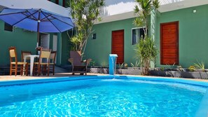 Une piscine avec un élément décoratif aquatique aux eaux bleues, entourée de mobilier d’extérieur et de plantes.