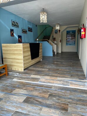 A hotel reception area with a wooden reception desk, a staircase, and a fire extinguisher on the wall.