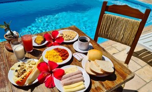 Una mesa con alimentos para el desayuno junto a una piscina, incluyendo platos de huevos, pan y una bebida.