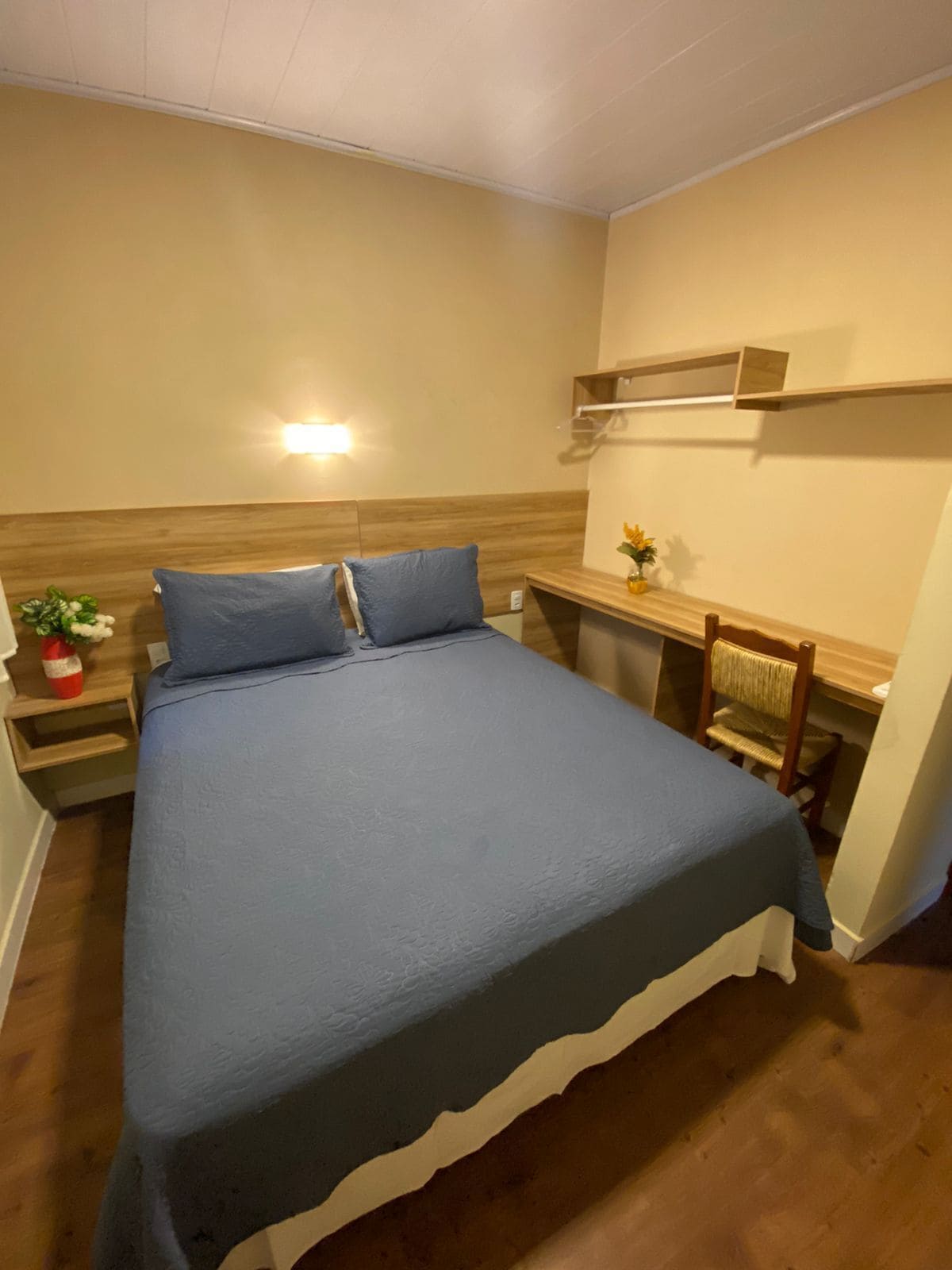 Een slaapkamer met een bed, nachtkastje, stoel, plank en een wandlamp.