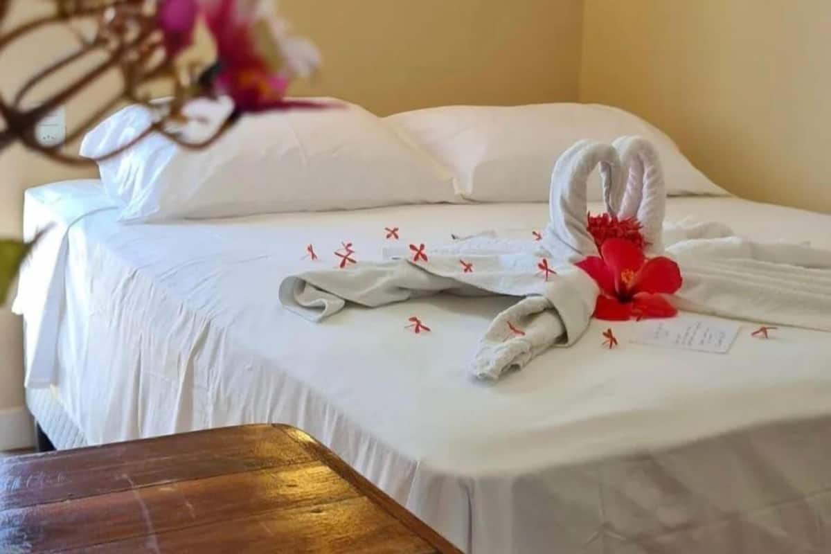 Siisti hotellihuone, jossa on huolitellusti pedattu sänky, puinen yöpöytä ja seinään kiinnitetty valaisin.