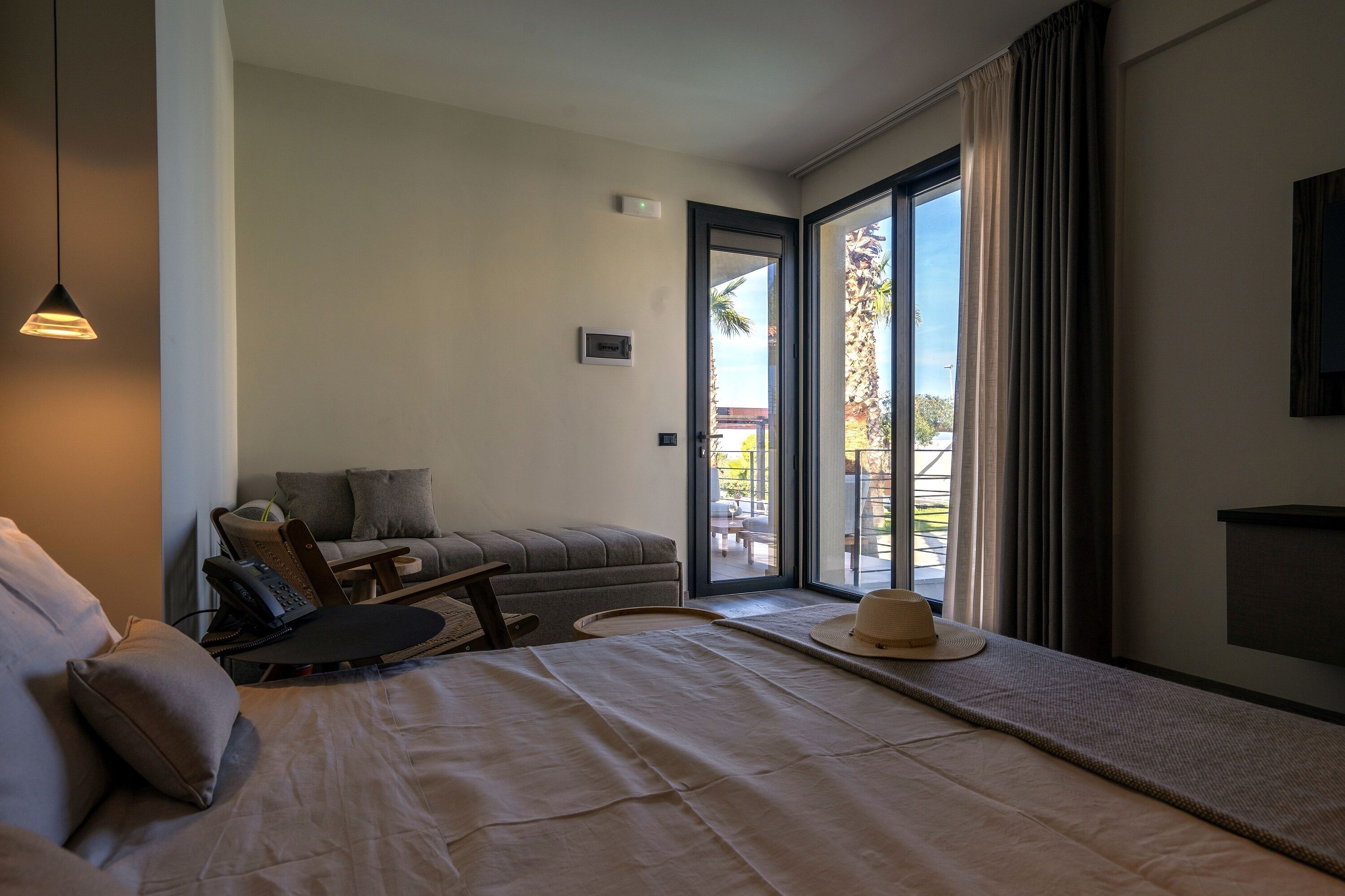 A hotel room with a bed, a sofa, a chair, a hat, and a view of the outdoors.