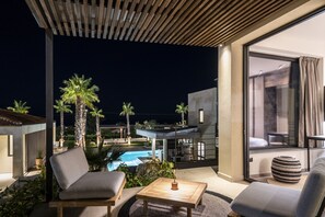 Un espace extérieur moderne aménagé avec des sièges, donnant sur la piscine, doté de mobilier en bois et d’une porte vitrée qui mène à un balcon.