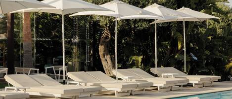 A pool area with lounge chairs and umbrellas, surrounded by palm trees and greenery.