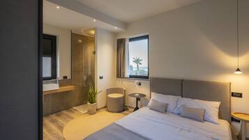 A modern bedroom with a large bed, a round rug, a small round table, a potted plant, and a view of palm trees through a window.
