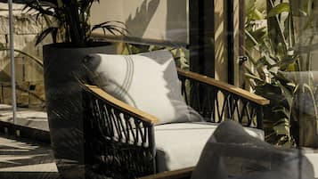 Un área de estar moderna al aire libre con una silla acolchada y una planta grande en maceta.