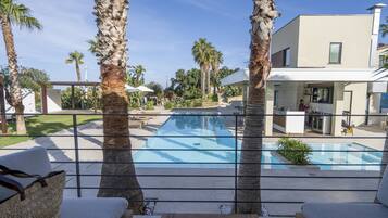 Un área de piscina exterior moderna con palmeras, una silla de descanso y un edificio contemporáneo al fondo.