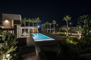 A modern hotel with a swimming pool, palm trees, and outdoor seating areas.