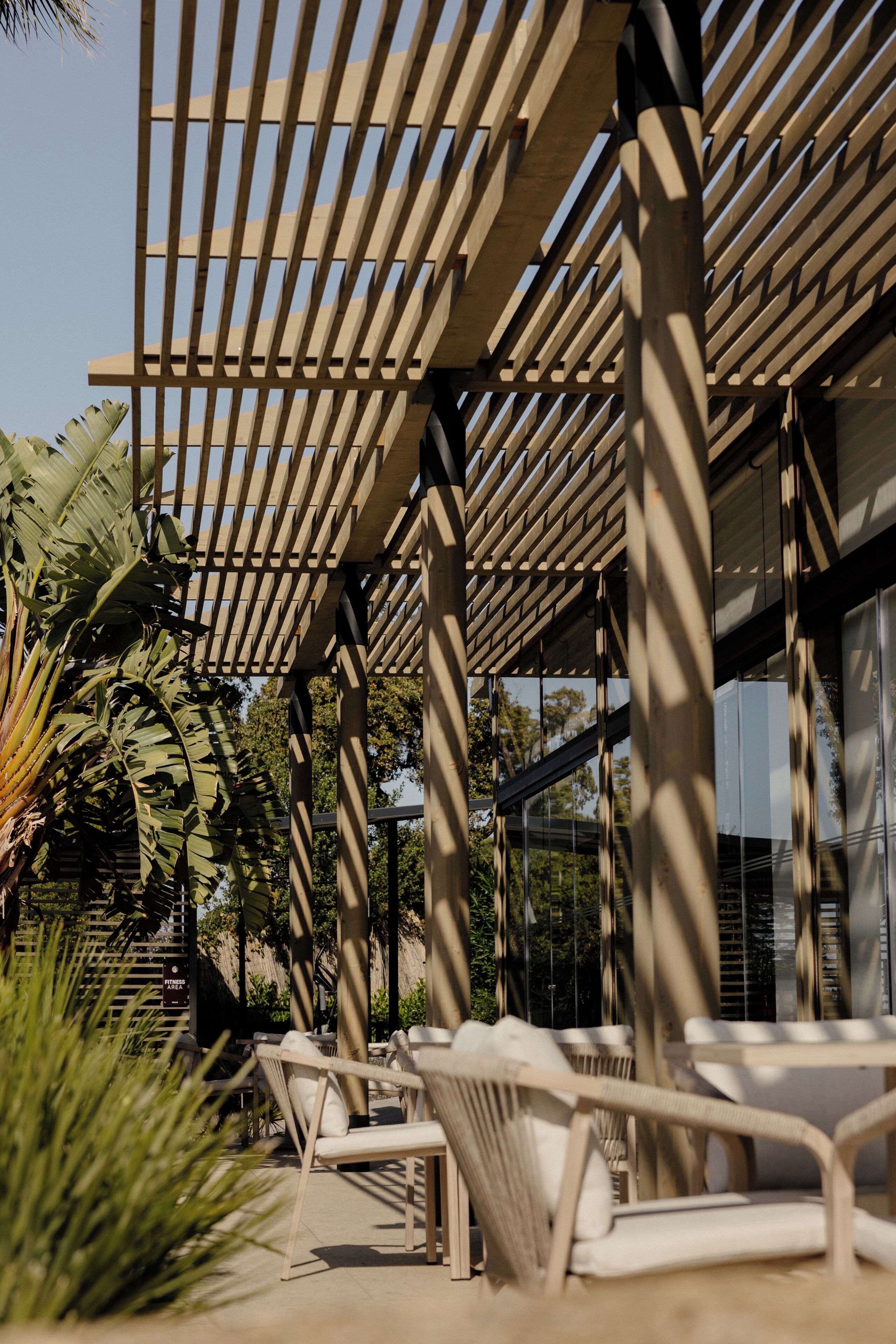 Un área de estar al aire libre con techo, muebles de madera y una estructura de pérgola.