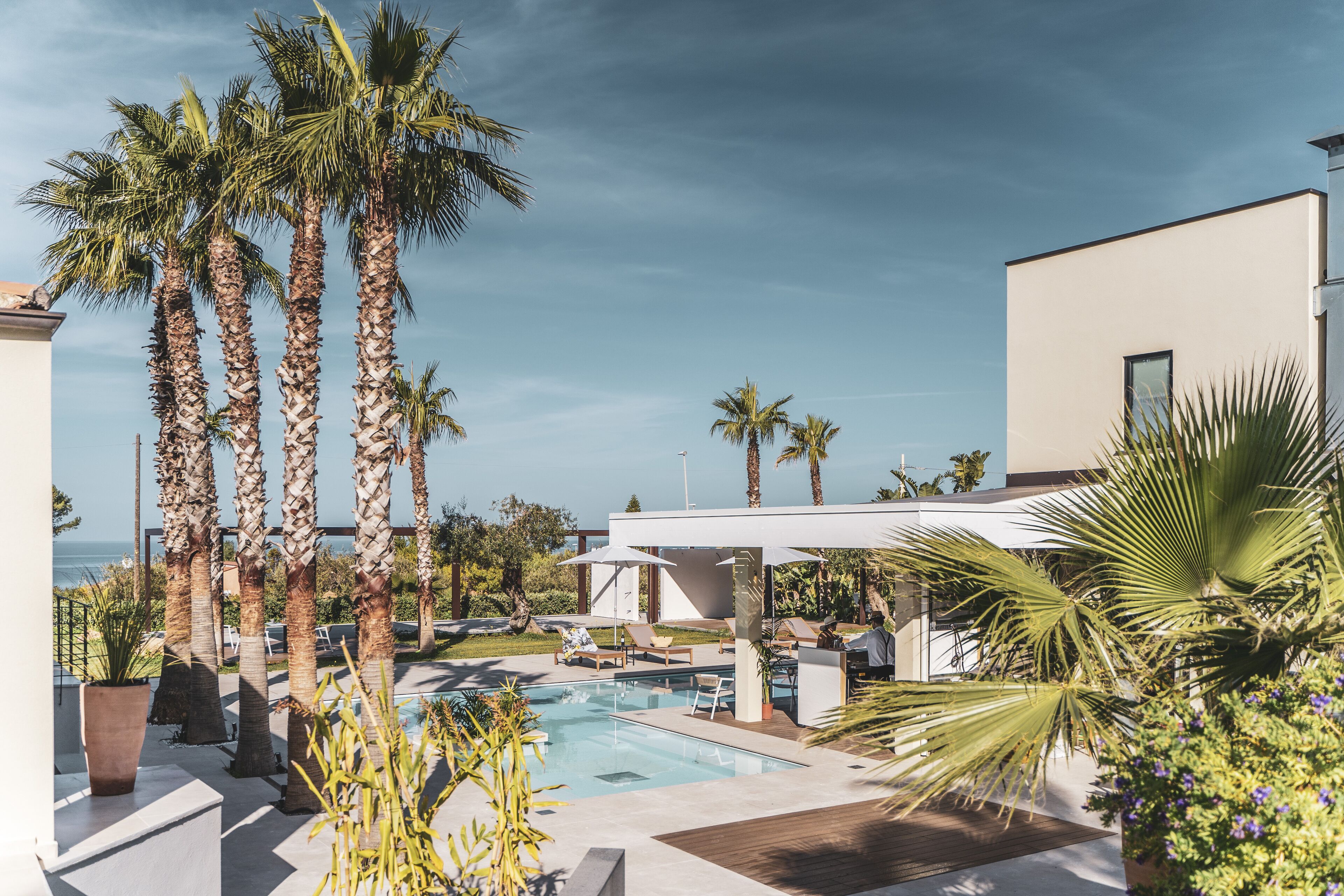 A pool area with palm trees, lounge chairs, and a view of the ocean.