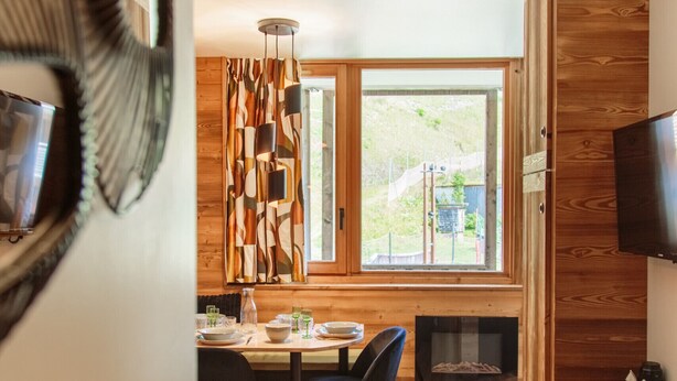 A modern dining area with a wooden table and chairs, a fireplace, and a large window with a view of greenery. - Immodreams - Le Billat - Avoriaz (Avoriaz)