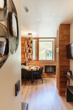 A modern dining area with a wooden table and chairs, a fireplace, and a large window with a view of greenery.