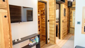 A modern interior with a wooden wall, a flat-screen TV mounted above a shelf with books and small figurines, and a wooden door leading to another room. - Immodreams - Le Billat - Avoriaz (Avoriaz)