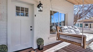 Une maison blanche en briques, avec un porche à l’avant, un banc suspendu, un pot de fleurs et une lanterne suspendue.