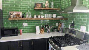 Une cuisine avec un dosseret de carrelage vert, des armoires noires, une cuisinière et divers ustensiles de cuisine disposés sur le plan de travail.