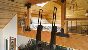 Une chambre de style loft avec un plafond en pente, des poutres en bois, un lit superposé, un puits de lumière et un attrape-rêves.