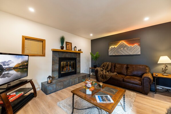 Una sala de estar moderna con chimenea, un sofá de cuero, un televisor de pantalla plana y una mesa de centro con objetos decorativos.