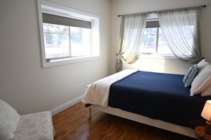 A bedroom with a bed, a window with curtains, a bedside table, and a lamp. - Tree To Me Inn (Keremeos)