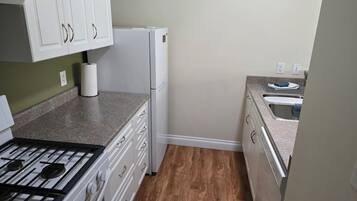 A compact kitchen with white cabinets, a gas stove, a refrigerator, and a sink.