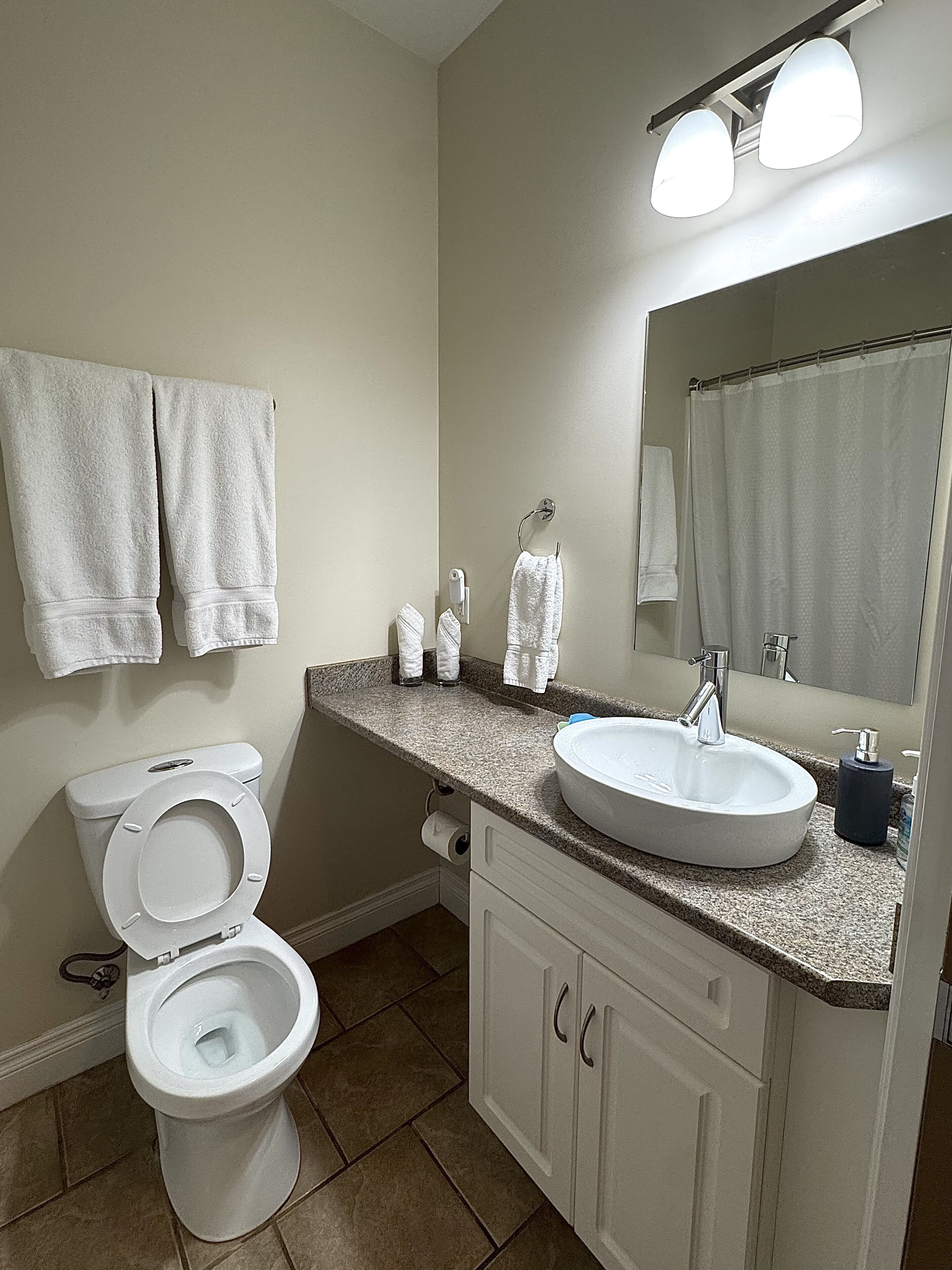 A bathroom with a toilet, sink, mirror, and two towels hanging on the wall.