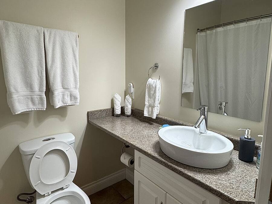 A bathroom with a toilet, sink, mirror, and two towels hanging on the wall.