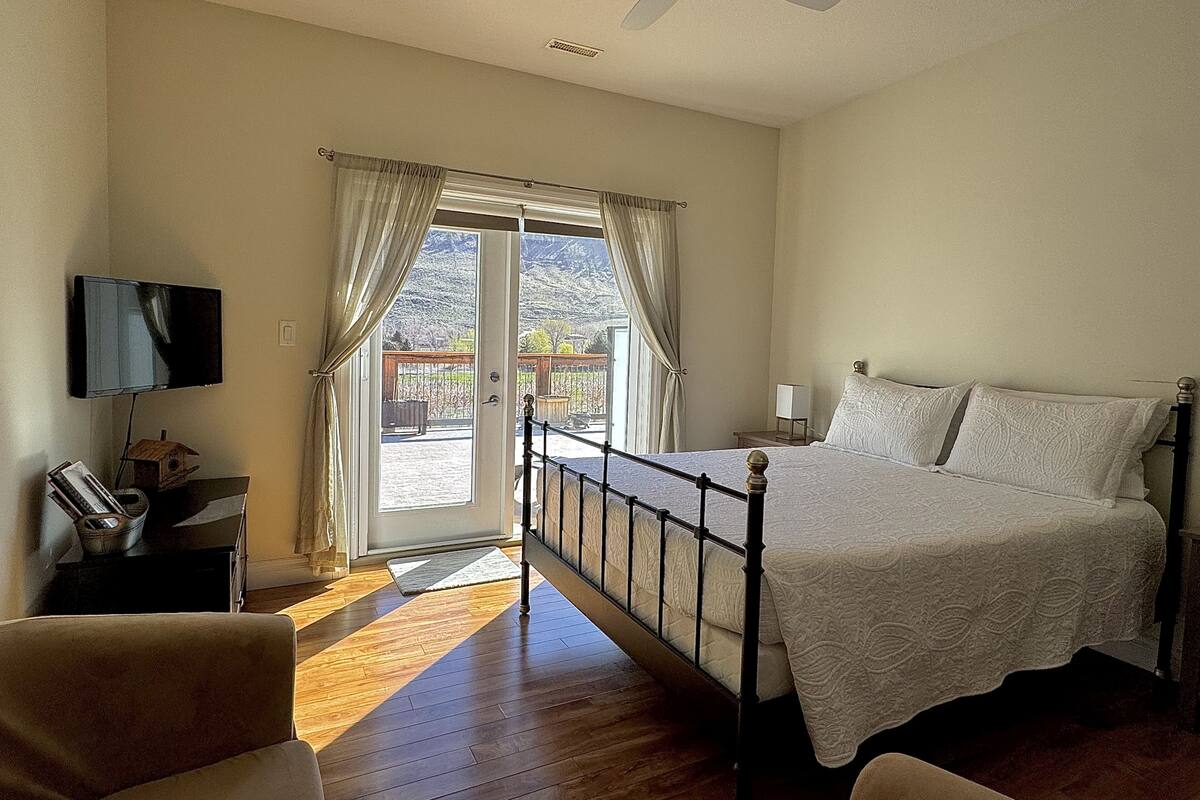A bedroom with a bed, a television, a desk, and a view through a door.