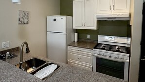 A kitchen with a stainless steel sink, white cabinets, a built-in oven, and a refrigerator.
