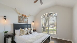A bedroom with a large bed, a world map artwork, a ceiling fan, and a window with blinds. - Rustic Aggie: 9 Min to Kyle Field + Pet-Friendly (Bryan)