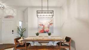 A dining area with a wooden table, two chairs, and a hanging light fixture above. - Rustic Aggie: 9 Min to Kyle Field + Pet-Friendly (Bryan)