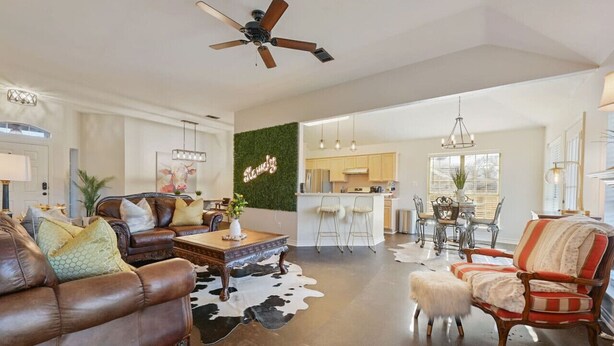 A spacious living room with a ceiling fan, a bar area, and a kitchen in the background. - Rustic Aggie: 9 Min to Kyle Field + Pet-Friendly (Bryan)