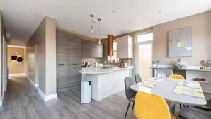 A modern kitchen with a central island, grey cabinets, and a dining area with a white table and yellow chairs. - Luxury London Garden Flat (London)