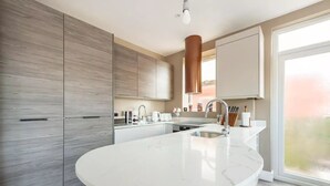 A modern kitchen with a large island, stainless steel appliances, and a large window providing natural light. - Luxury London Garden Flat (London)