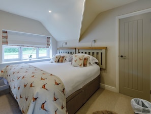 A bedroom with a large bed, a window with curtains, a bedside table, and a door.