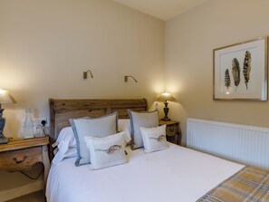 A neatly made bed with striped and plain pillows, a wooden headboard, bedside lamps, and a framed artwork on the wall.
