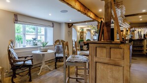A rustic interior with wooden beams, a dining area with chairs and a table, and a bar area with glasses.