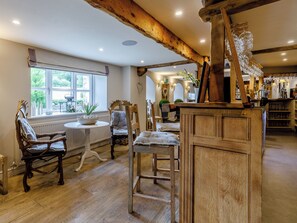A rustic interior with wooden beams, a dining area with chairs and a table, and a bar area with glasses.