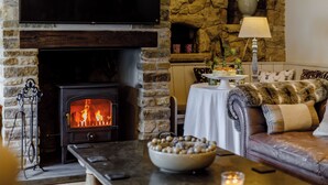 A cozy living room with a stone fireplace, a flat-screen TV, a leather sofa, and a dining table with a vase of flowers.