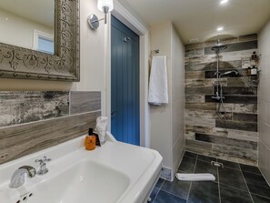 A bathroom with a white bathtub, a shower with a rain showerhead, and a blue door.