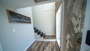 Een trap met houten treden die leidt naar een plateau, een muur met een bord waarop 'Hello and welcome' staat, en een gedeeltelijk beschadigde muur aan de rechterkant.