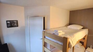 Una habitación pequeña con una cama individual de madera, una mesita de noche, una silla y una puerta.