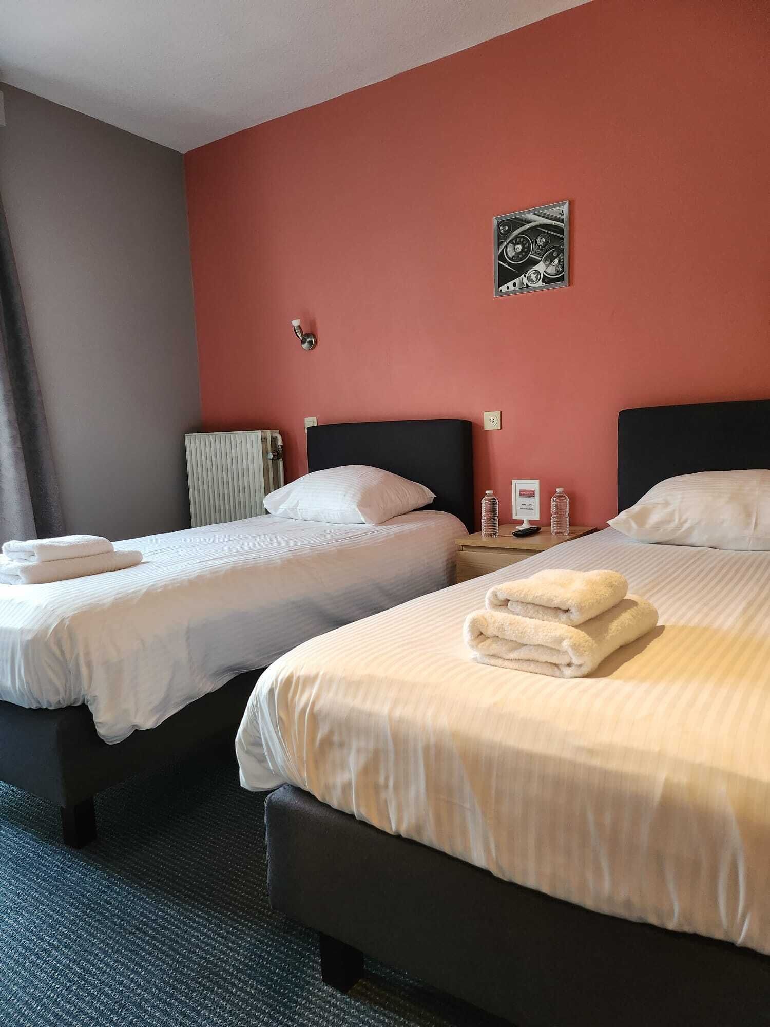 A hotel room with two beds, a radiator, a wall clock, and a framed picture.