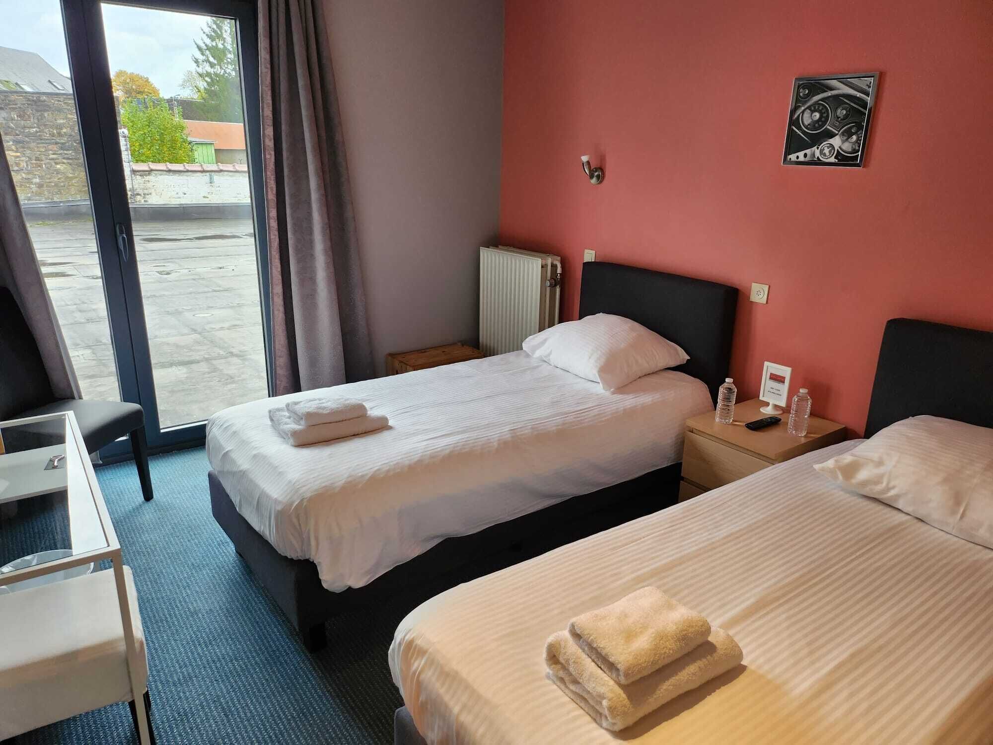 A hotel room with two beds, a desk, and a window with curtains.