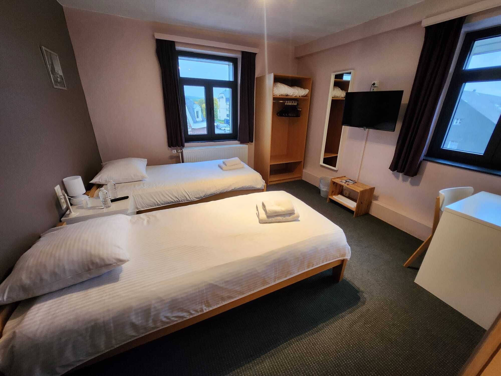A hotel room with two beds, a wardrobe, a television, and a desk.