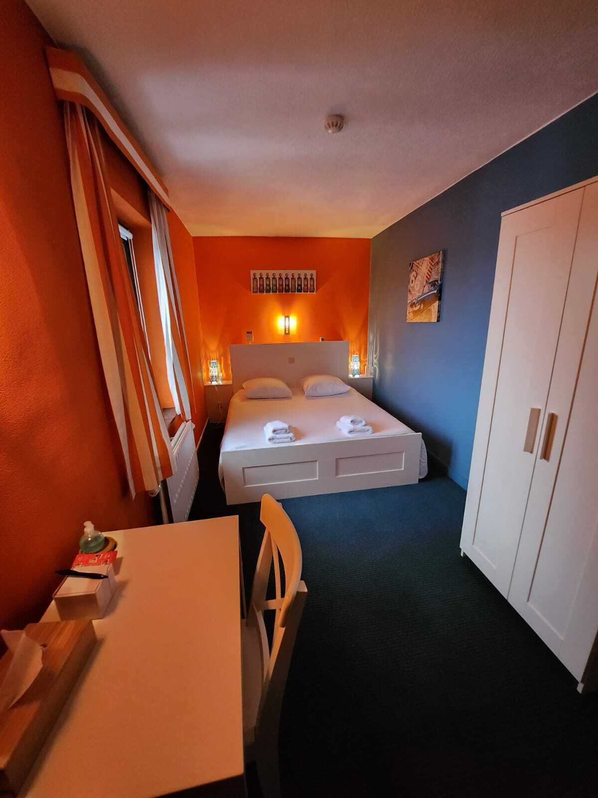 A hotel room with a bed, a desk, a chair, and a wardrobe.